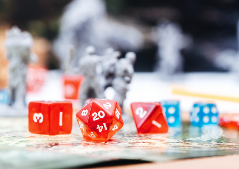 czerwone i turkusowe kości do gier RPG na jasnym blacie. W tle figurki.